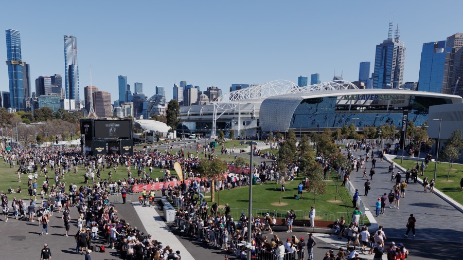 Crowd of people gathered outside of stadiums with large screen in centre to watch football match.