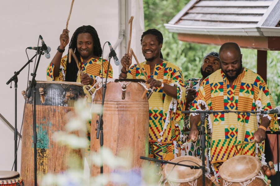 Three people playing African drums on a stage with microphones.