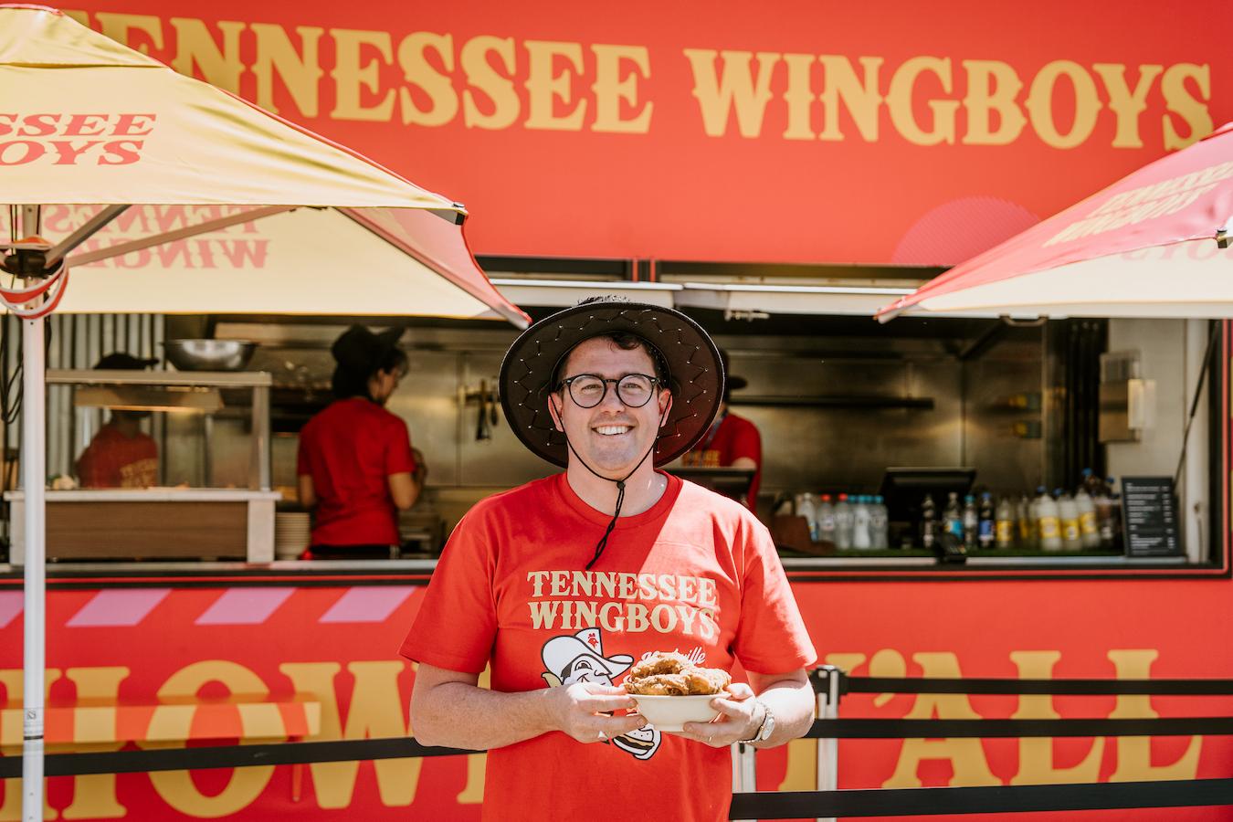 Charlie, founder Atlas Dining wearing a hat and red t shirt Tennessee Wingboys, in front of the Tennessee Wingboy food truck, background young people working in the food truck. at Australia Open 2025