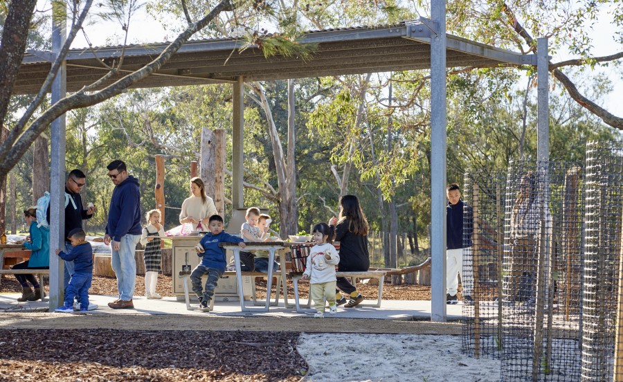 Adults and children standing in park eating area eating food.