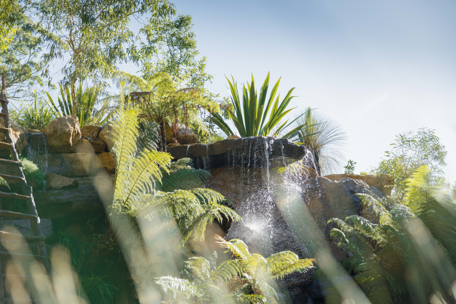 Waterfall feature over large rock surface surrounded by greenery.